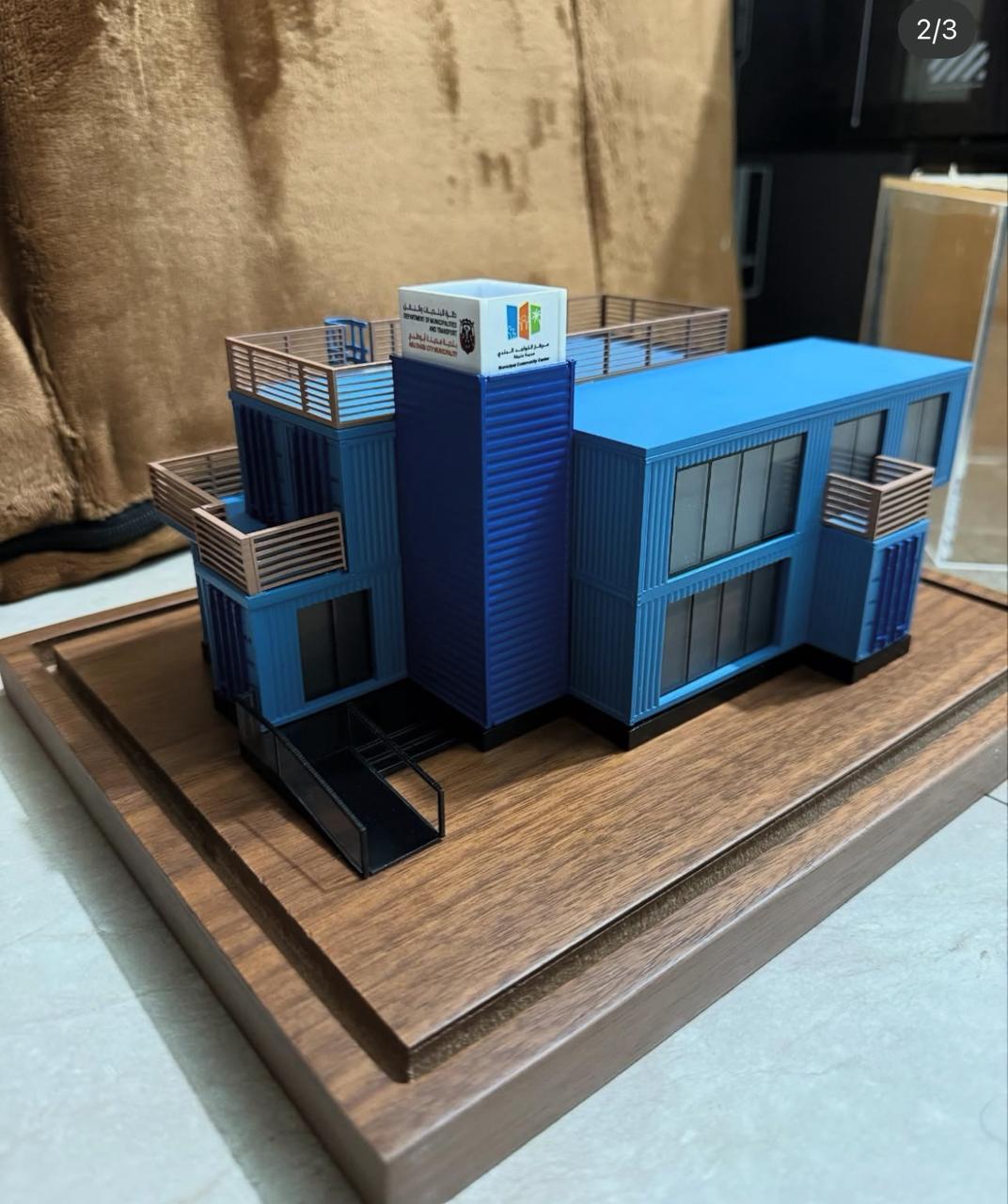Detailed blue building model with balconies and railings on a wooden display base