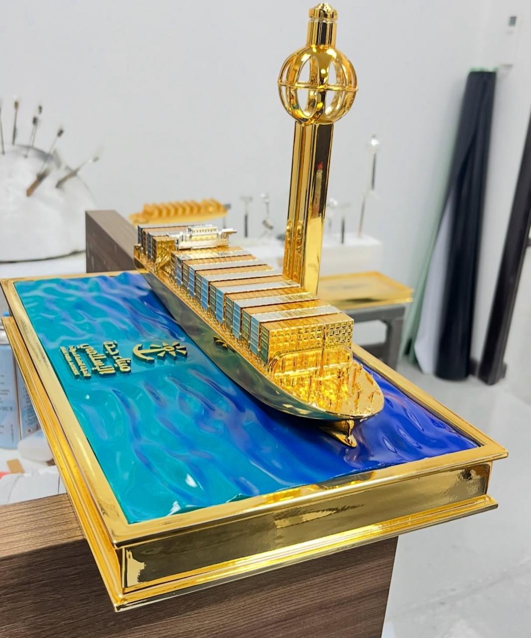 Gold-toned cargo ship and tower model on a blue sea-effect presentation base