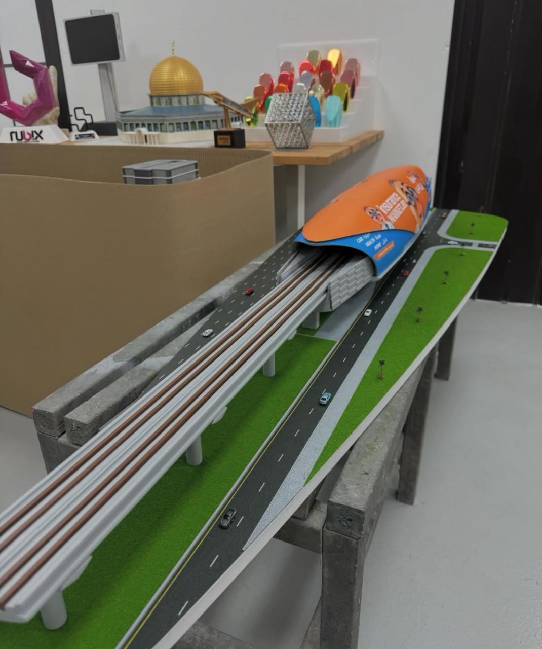 Scale model of an elevated rail station with tracks, roads and landscaping