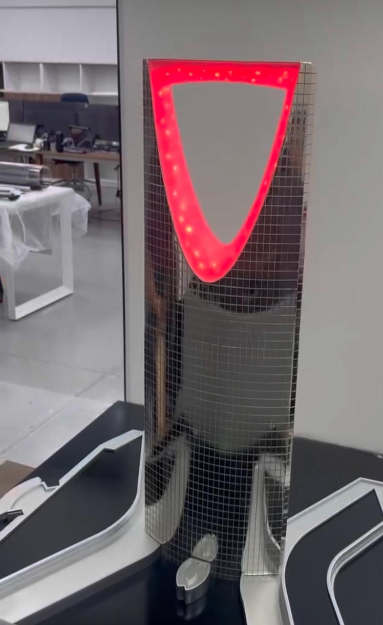 Tall architectural tower model with illuminated red upper opening